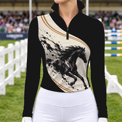 Woman wearing the black long sleeve quarter zip riding top with cream horse print panel and white riding breeches in a show jumping arena