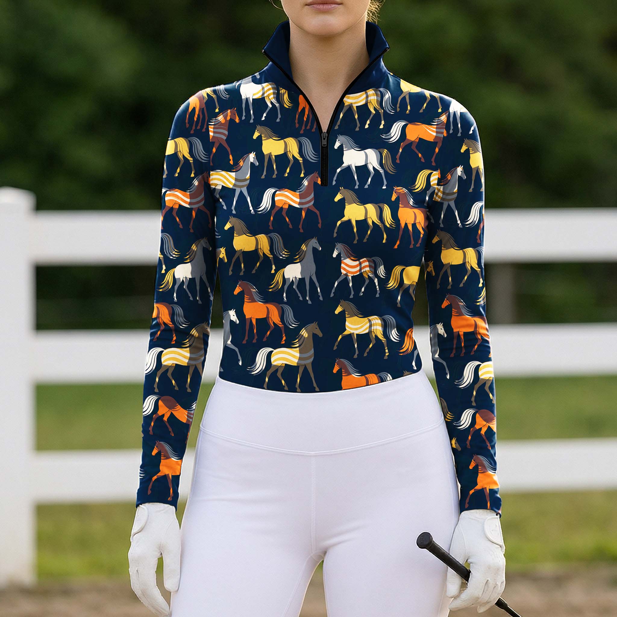 Navy blue horse print long sleeve quarter zip riding top styled with white breeches, white gloves, and a black crop in an outdoor arena with a white fence and green foliage