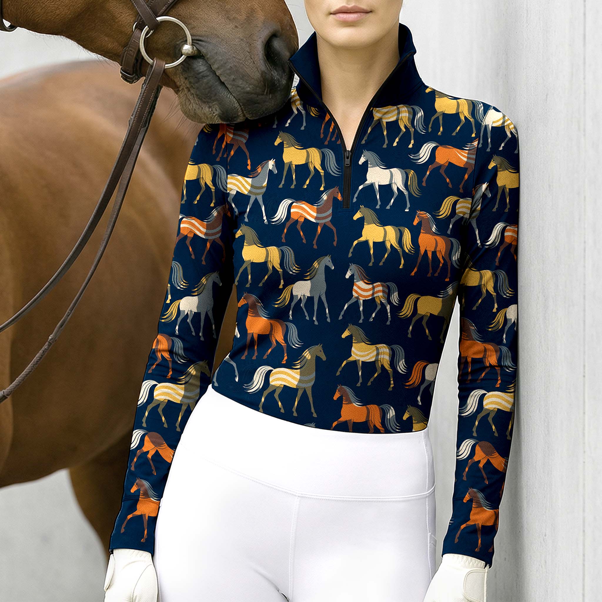 Navy blue horse print long sleeve quarter zip riding top styled with white breeches and white gloves, next to a brown horse with a leather bridle against a white wall