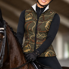 Woman wearing the olive stirrup and chain print side of the reversible quilted vest over a black long sleeve base layer with black breeches and gloves beside a dark bay horse