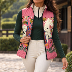 Pink reversible quilted equestrian vest with horse and floral print worn open over a dark green long sleeve quarter zip top and white riding breeches