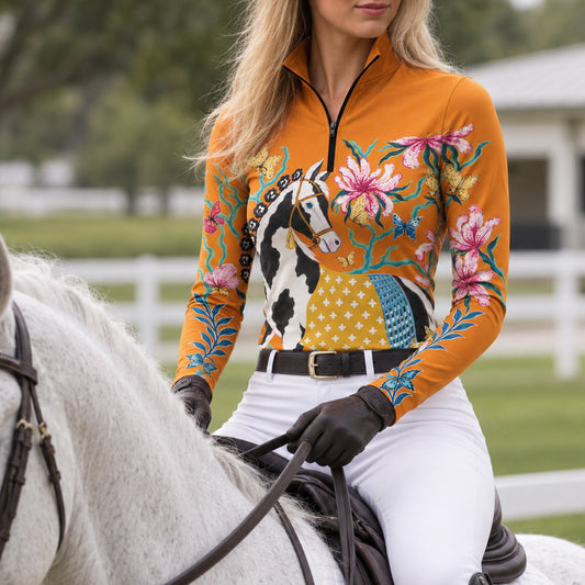Rider wearing the orange pinto horse print riding top with white breeches and a leather belt while mounted on a gray horse