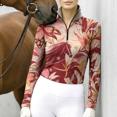 Woman wearing the cream horse and butterfly print quarter zip riding top with breeches and a leather belt while standing with a chestnut horse
