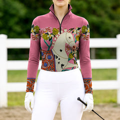 Woman wearing RIDER ATELIER artisan Dala horse dusty rose equestrian quarter-zip top at the outdoor pasture