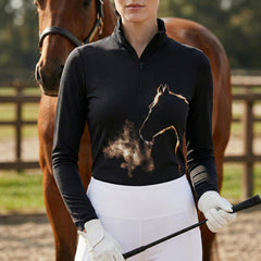 Woman wearing black equestrian golden smoke horse silhouette print long sleeve zip top standing beside a chestnut horse at the stable
