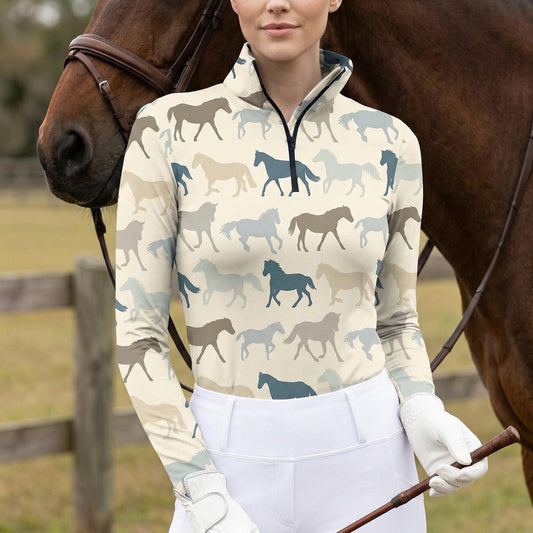 Woman wearing cream equestrian wild herd silhouette print long sleeve zip top standing beside a chestnut horse at the stable