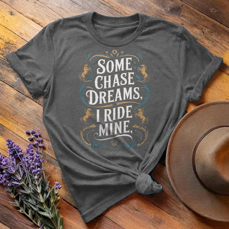 Dark gray "Some Chase Dreams, I Ride Mine" equestrian t-shirt, flat lay on wooden background