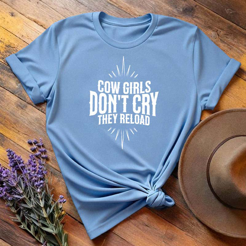 Light blue "Cow Girls Don't Cry They Reload" western equestrian t-shirt, flat lay on wooden background