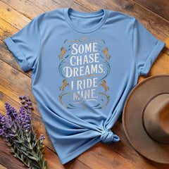Light blue "Some Chase Dreams, I Ride Mine" equestrian t-shirt, flat lay on wooden background