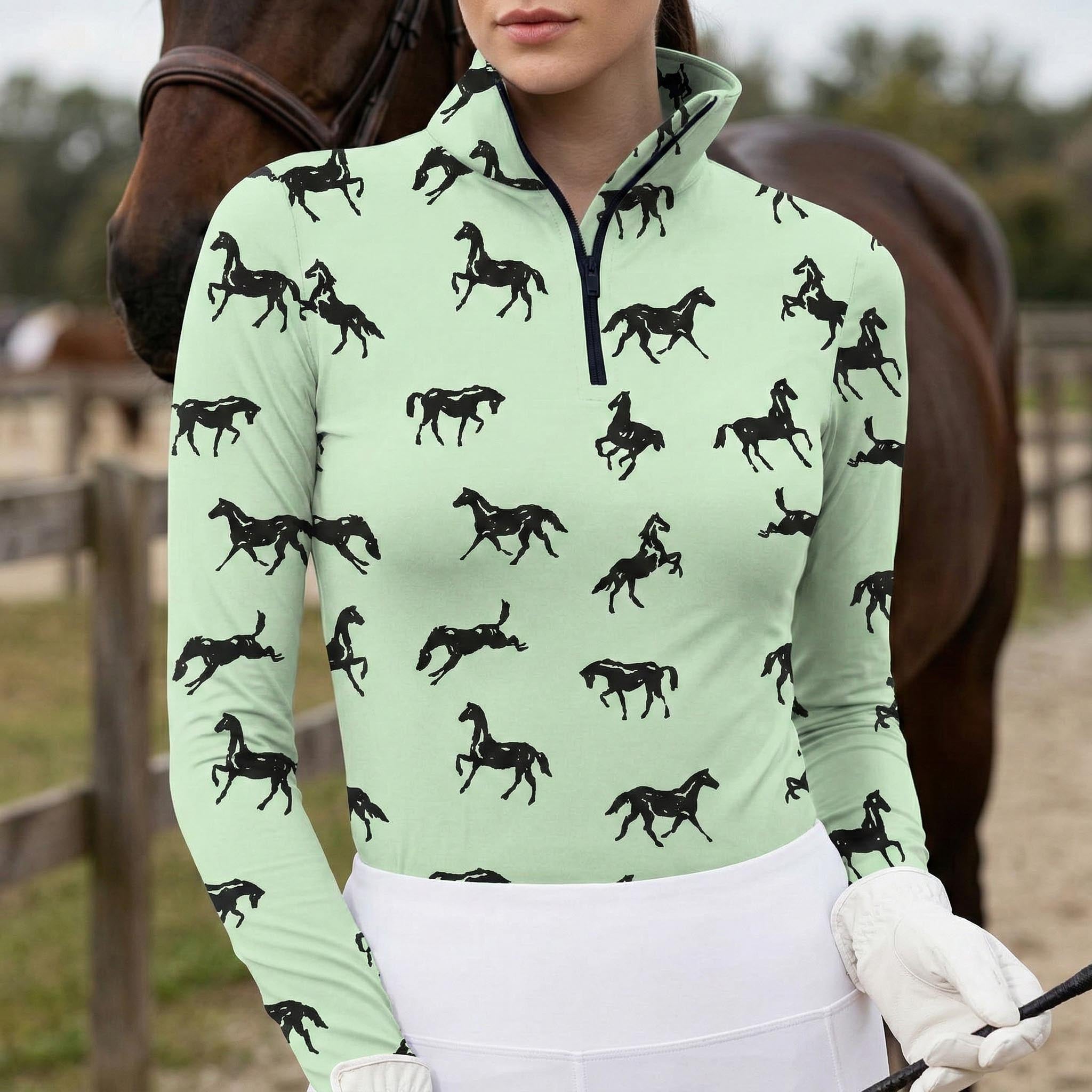 Woman wearing mint green equestrian galloping horse silhouette print long sleeve zip top standing beside a chestnut horse at the stable