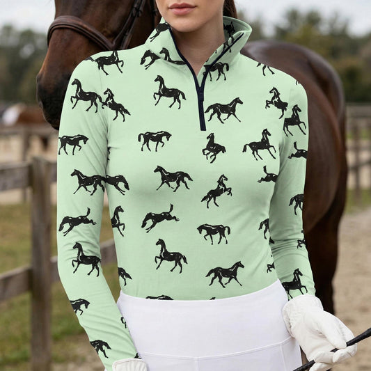 Woman wearing mint green equestrian galloping horse silhouette print long sleeve zip top standing beside a chestnut horse at the stable