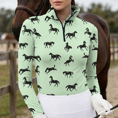 Woman wearing mint green equestrian galloping horse silhouette print long sleeve zip top standing beside a chestnut horse at the stable