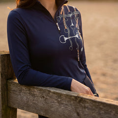 Side view of woman wearing navy equestrian tack bouquet print quarter-zip top leaning on wooden stable fence