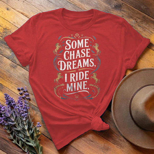 Red "Some Chase Dreams, I Ride Mine" equestrian t-shirt, flat lay on wooden background
