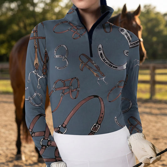 Woman wearing slate blue equestrian bridle and horseshoe print long sleeve zip top standing beside a horse at the stable