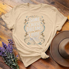 Tan "Some Chase Dreams, I Ride Mine" equestrian t-shirt, flat lay on wooden background