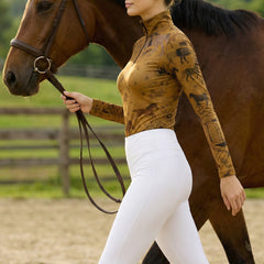 Woman walking chestnut horse while wearing tan vintage equestrian allover print quarter-zip riding top at the arena