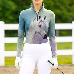 Woman wearing RIDER ATELIER watercolor white horse ombre teal-purple equestrian quarter-zip top at the outdoor pasture