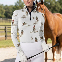 Woman wearing white equestrian fox hunt scene print long sleeve zip top standing beside a chestnut horse at the stable