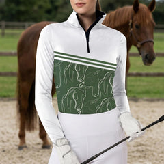 Woman wearing white and green equine line art stripe print long sleeve zip top standing beside a chestnut horse at the stable