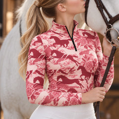 Woman wearing the light pink floral horse print quarter zip riding top next to a white horse with a brown leather bridle