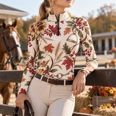 Woman wearing the cream printed long sleeve quarter zip riding top with beige breeches and a brown belt beside a brown horse with white facial markings