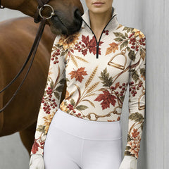 Woman wearing the cream printed long sleeve quarter zip riding top with beige breeches and a brown belt near a stable and autumn decor