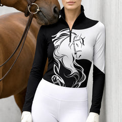 Woman wearing the black and white two horse head riding top next to a brown horse with a leather bridle against a light gray wall