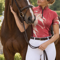 Pink short sleeve riding top with white horse print worn near a brown horse in a grassy equestrian setting